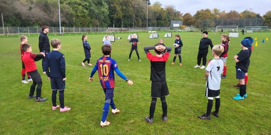 Kinder stehen im Kreis beim Fußballtraining auf dem Sportplatz.