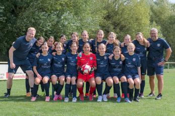 Mädchen-Fußballteam posiert mit Trainern für Mannschaftsfoto auf dem Sportplatz.