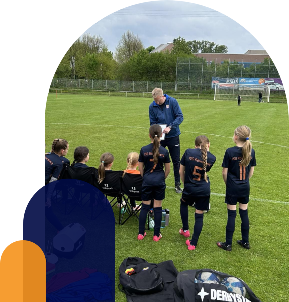 Trainer bespricht Taktik mit Mädchen-Fußballteam am Spielfeldrand.