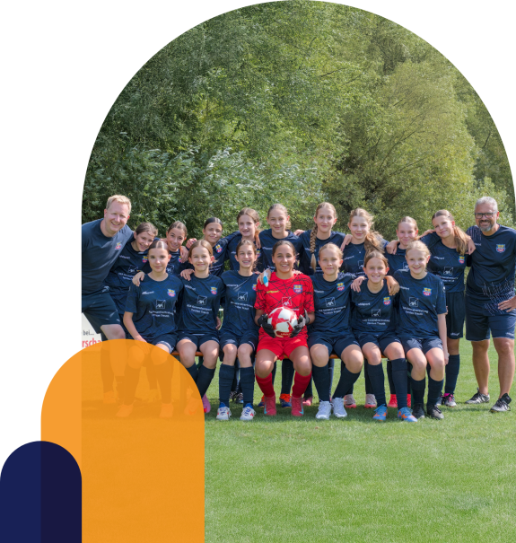 Mädchen-Fußballmannschaft mit Trainern posiert für Gruppenfoto auf dem Sportplatz.